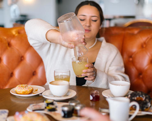 Woman sitting at a large round table pouring some juice from a jug 