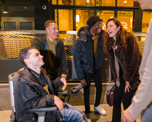 A group of young adults talking and laughing outside a venue in coats and hats