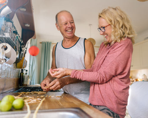 A couple of people laughing while preparing food on their home counter top
