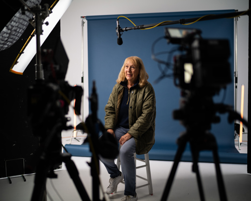 An older white woman talking to a camera with recording equipment set up around her