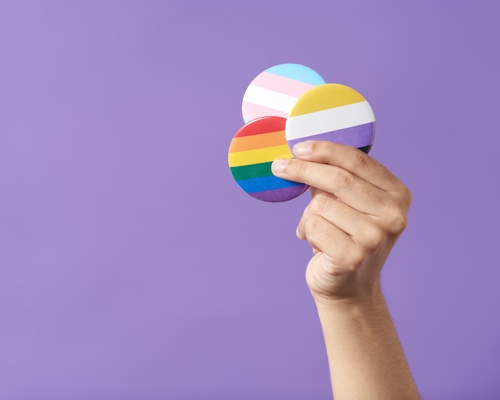 A person holding up pins with the transgender, non-binary and LGBT+ flags